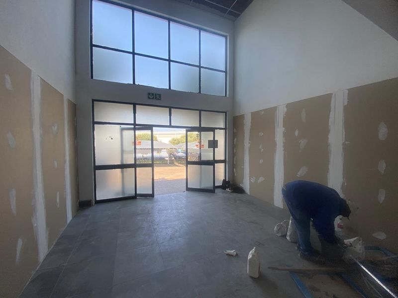 Industrial entrance area featuring high ceilings, large glass windows, and tiled flooring, currently undergoing final wall finishing and interior fit-out.