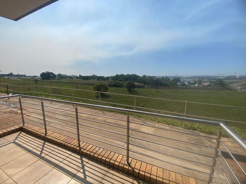 An elevated balcony featuring a stainless steel balustrade, tiled flooring, and brick edging, offering expansive views over the surrounding landscape.
