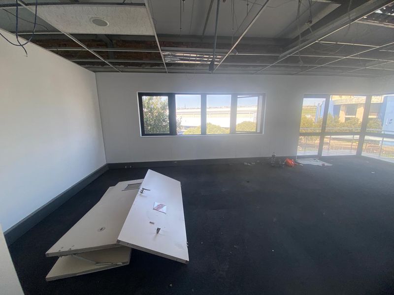 An industrial office space featuring a suspended ceiling grid, carpeted flooring, and large windows, currently requiring ceiling repairs and general maintenance.