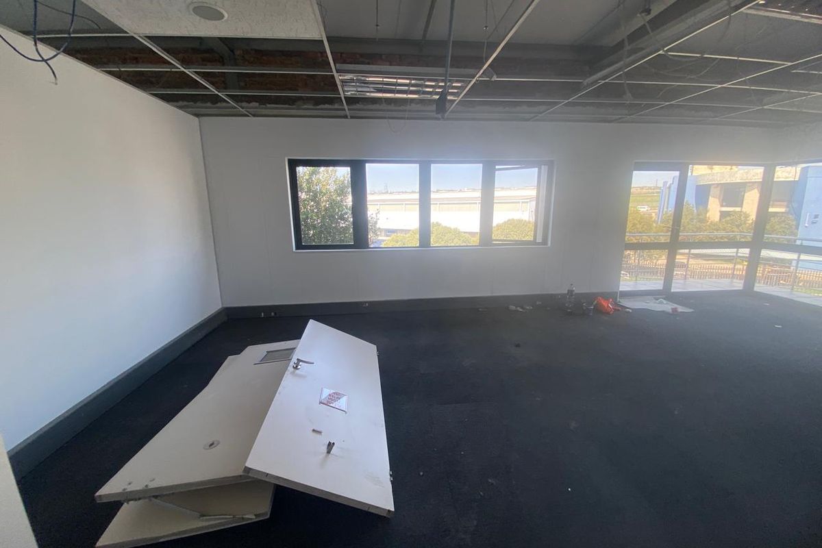 An industrial office space featuring a suspended ceiling grid, carpeted flooring, and large windows, currently requiring ceiling repairs and general maintenance.