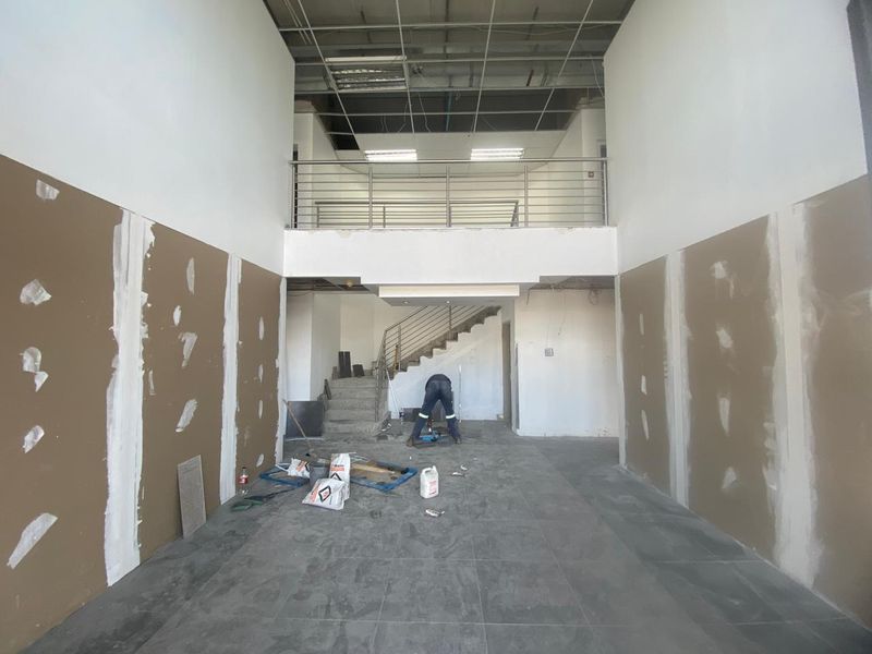 An industrial open-plan space currently under renovation, featuring a mezzanine level, staircase, and unfinished wall and ceiling finishes.