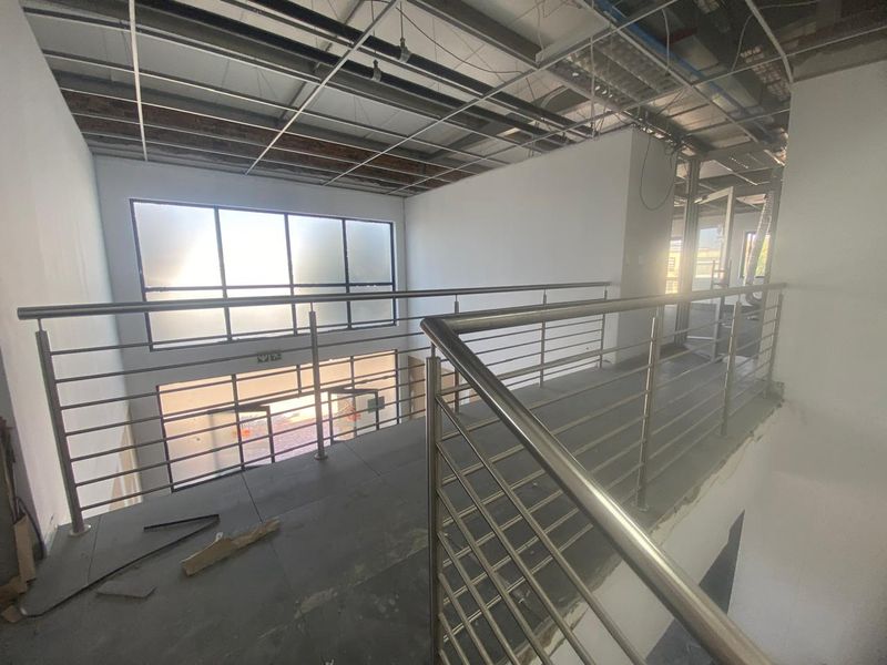 An unfinished industrial mezzanine hallway featuring stainless steel balustrades, tiled flooring, and exposed ceiling infrastructure, currently in a shell condition.
