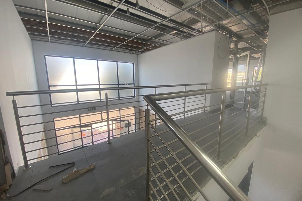 An unfinished industrial mezzanine hallway featuring stainless steel balustrades, tiled flooring, and exposed ceiling infrastructure, currently in a shell condition.