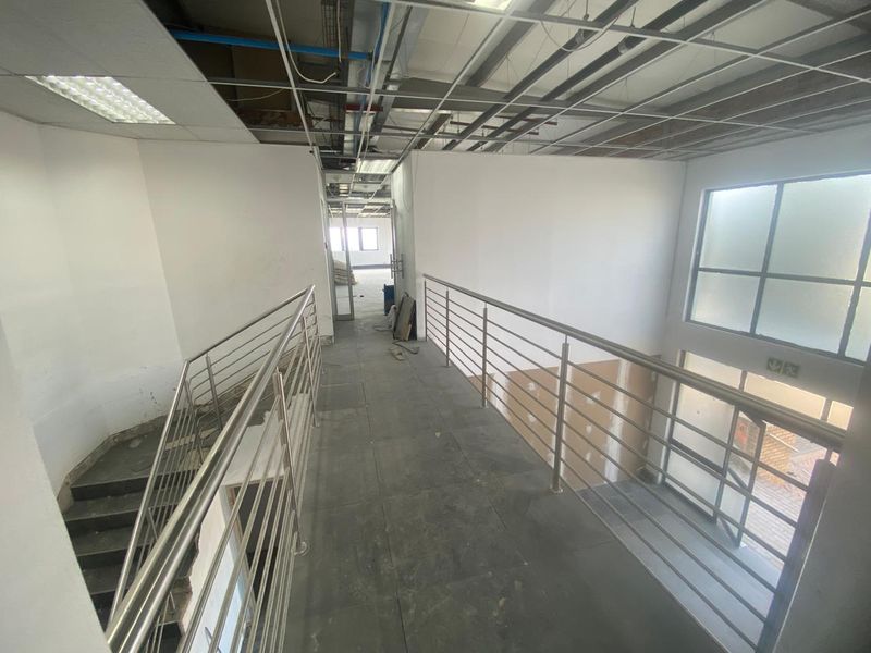 An industrial-style hallway featuring a stainless steel balustrade, tiled flooring, and an unfinished ceiling with exposed infrastructure, currently in a shell condition.