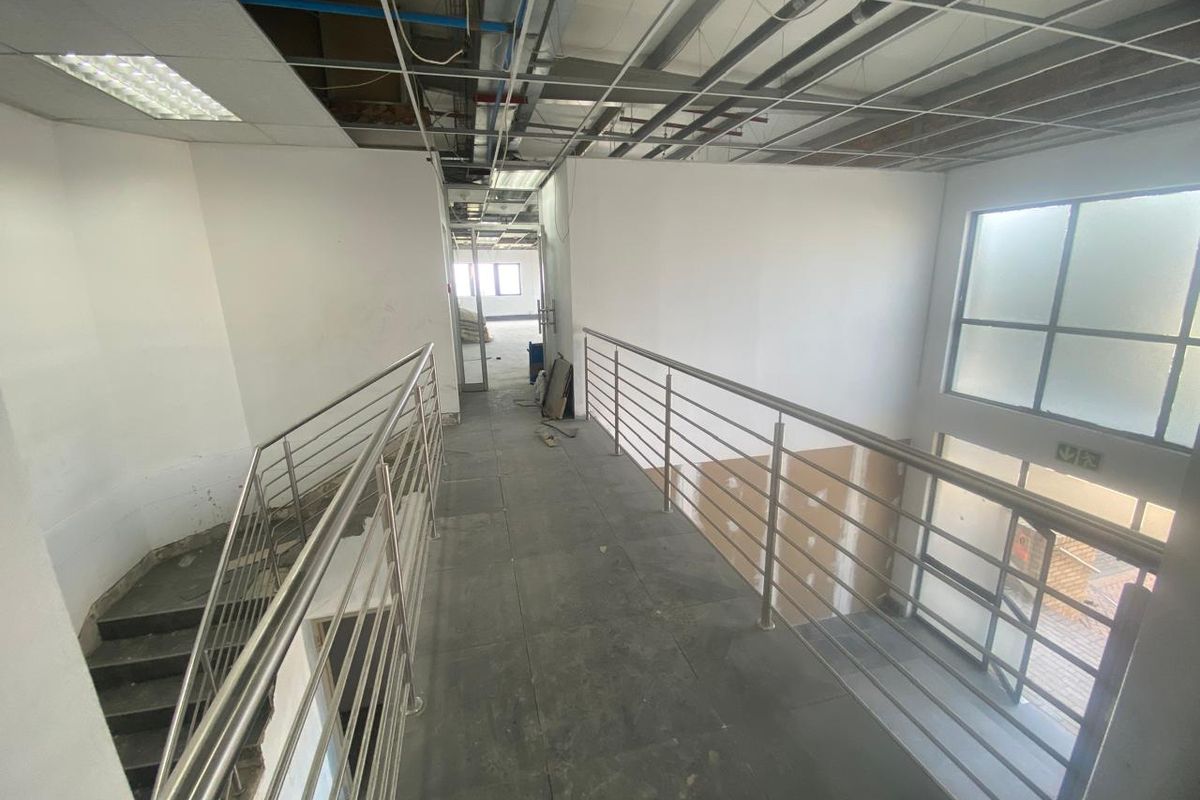 An industrial-style hallway featuring a stainless steel balustrade, tiled flooring, and an unfinished ceiling with exposed infrastructure, currently in a shell condition.
