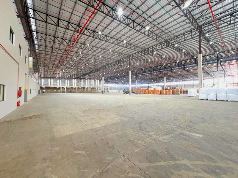 Expansive industrial warehouse space featuring high ceilings with exposed steel trusses, fire sprinkler systems, high bay lighting, and durable concrete flooring.