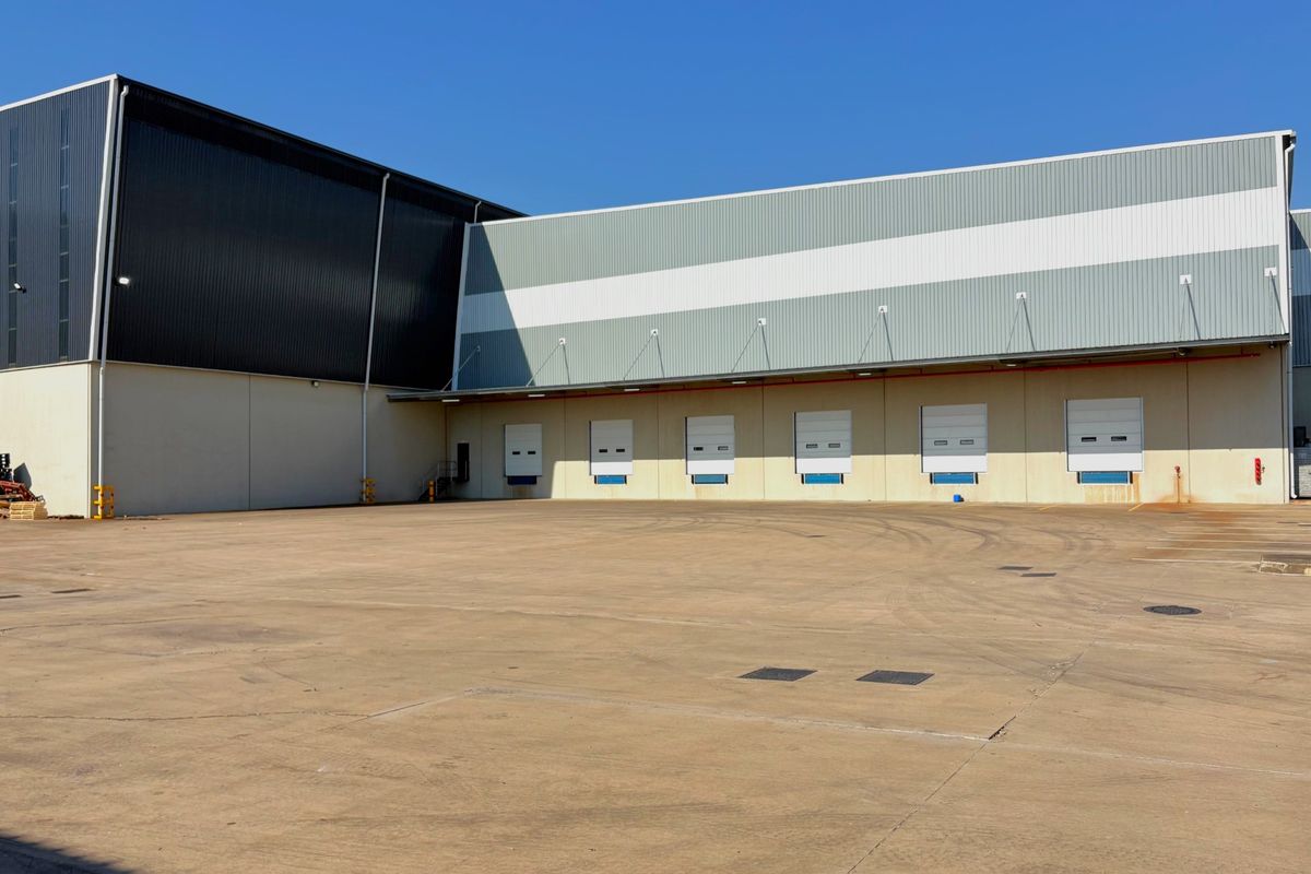 Industrial warehouse exterior featuring multiple loading docks with roller shutter doors and a large concrete yard area for logistics and transport access.