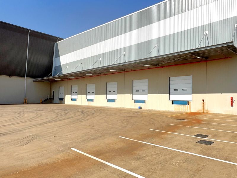Industrial warehouse exterior featuring multiple loading docks with roller shutter doors, a covered canopy, and a spacious concrete yard area.