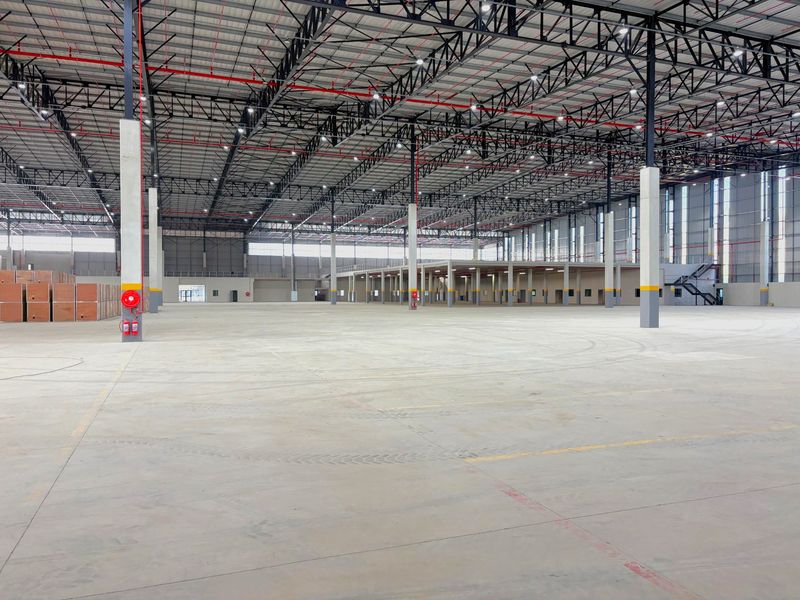 Expansive industrial warehouse space featuring high ceilings with exposed steel trusses, polished concrete flooring, integrated fire suppression systems, and a mezzanine level.