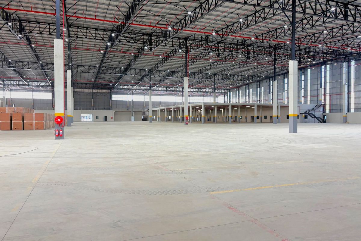 Expansive industrial warehouse space featuring high ceilings with exposed steel trusses, polished concrete flooring, integrated fire suppression systems, and a mezzanine level.