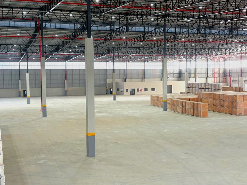 Spacious industrial warehouse featuring high ceilings with exposed steel trusses, fire sprinkler system, polished concrete floors, and integrated internal office space.
