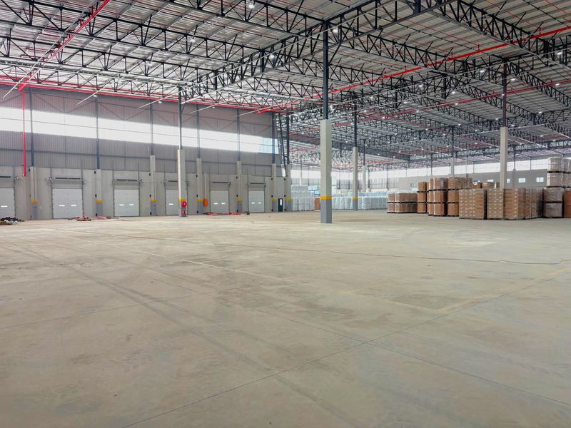 Spacious industrial warehouse featuring high ceilings with exposed steel trusses, concrete flooring, fire sprinkler system, and multiple loading bay doors.