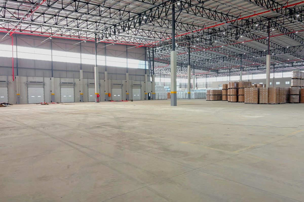 Spacious industrial warehouse featuring high ceilings with exposed steel trusses, concrete flooring, fire sprinkler system, and multiple loading bay doors.