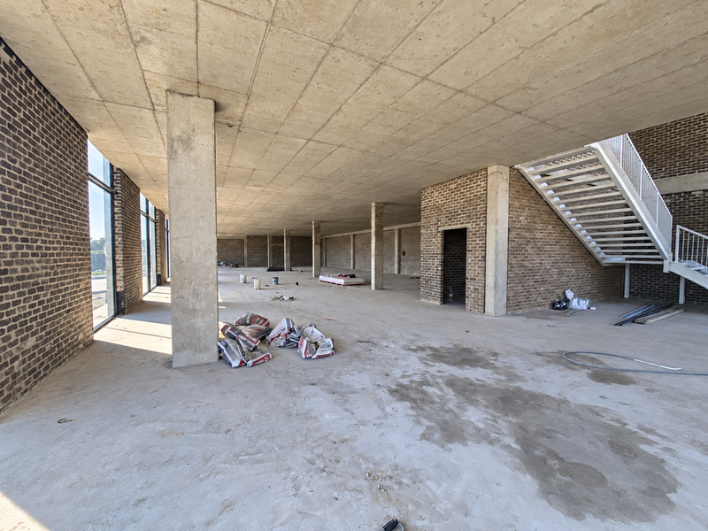 Spacious industrial open-plan area featuring exposed brick walls, concrete ceilings, and a modern metal staircase, currently in an unfinished construction state.