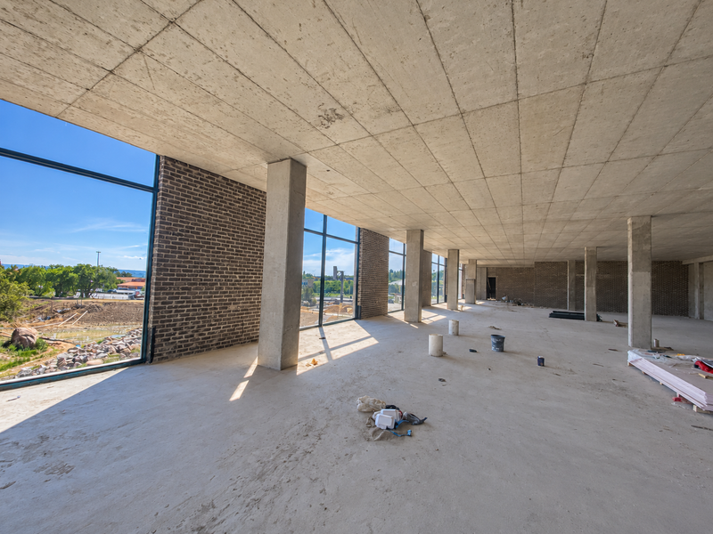 Spacious open-plan industrial interior featuring exposed concrete ceilings, structural columns, brick walls, and expansive windows with natural light.