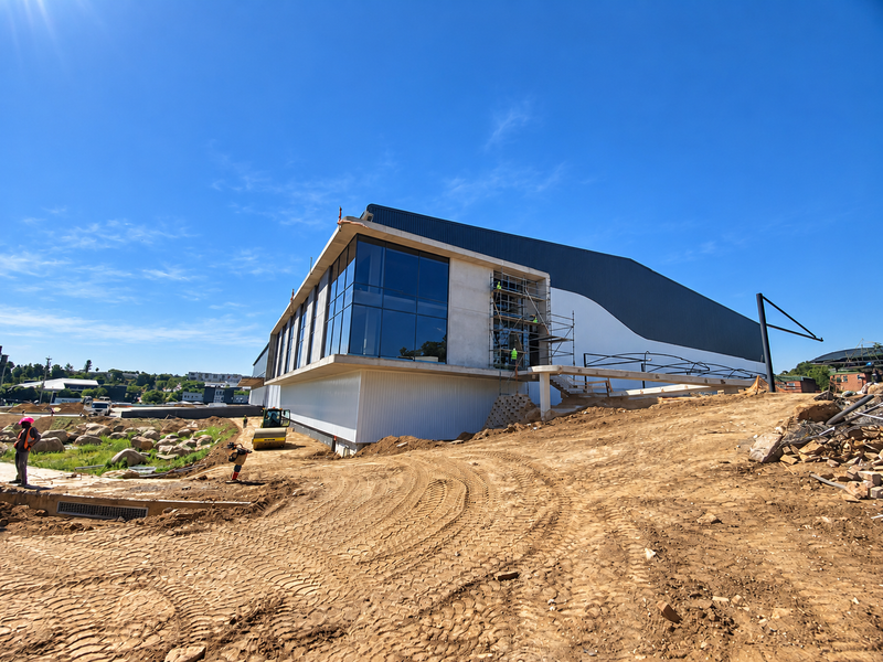 Rear view of an industrial building under construction, featuring large glass panels, metal cladding, and ongoing site development.