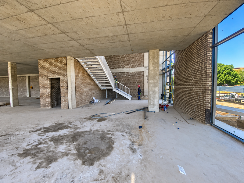 Spacious industrial open-plan area under construction featuring exposed brickwork, concrete ceilings, a modern steel staircase, and expansive floor-to-ceiling glass windows.