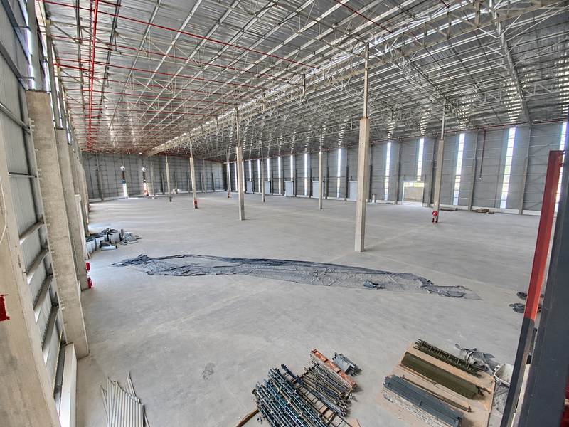 A large, open-plan industrial warehouse space featuring high ceilings with exposed steel trusses, concrete flooring, and integrated fire sprinkler systems.