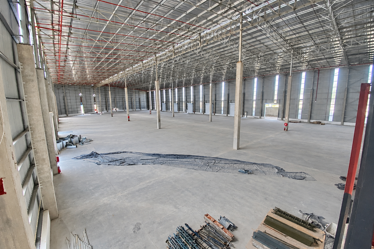 A large, open-plan industrial warehouse space featuring high ceilings with exposed steel trusses, concrete flooring, and integrated fire sprinkler systems.
