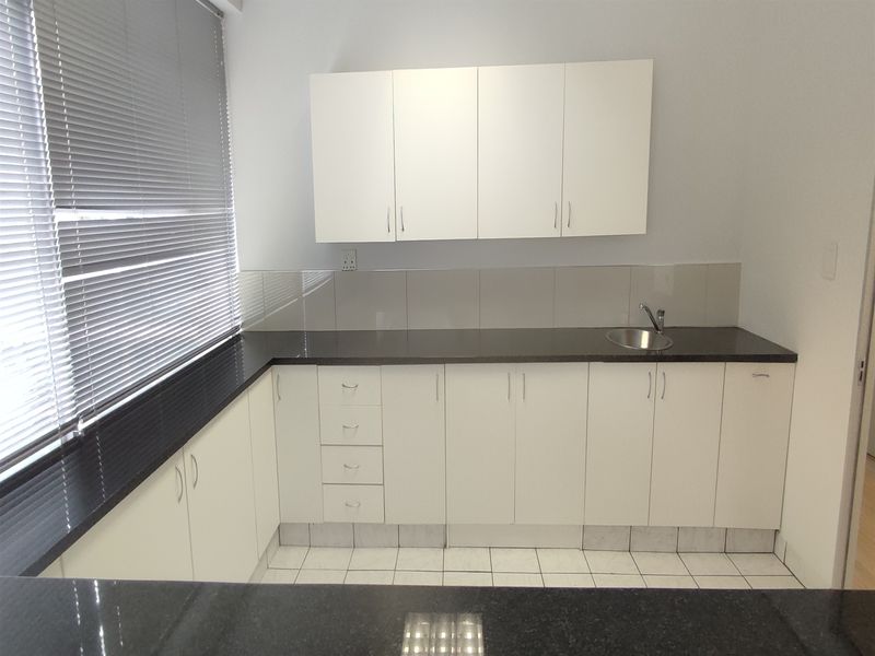 A clean and functional office kitchenette featuring white cabinetry, dark granite countertops, a stainless steel sink, and a tiled backsplash.