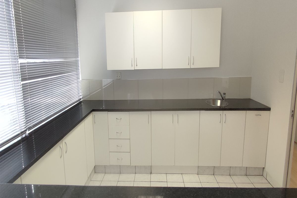 A clean and functional office kitchenette featuring white cabinetry, dark granite countertops, a stainless steel sink, and a tiled backsplash.