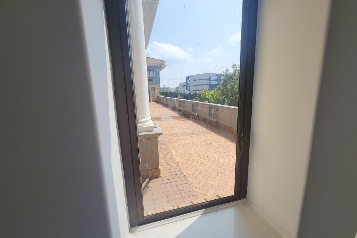 View from an interior window looking out onto a paved balcony area with a balustrade and structural column.