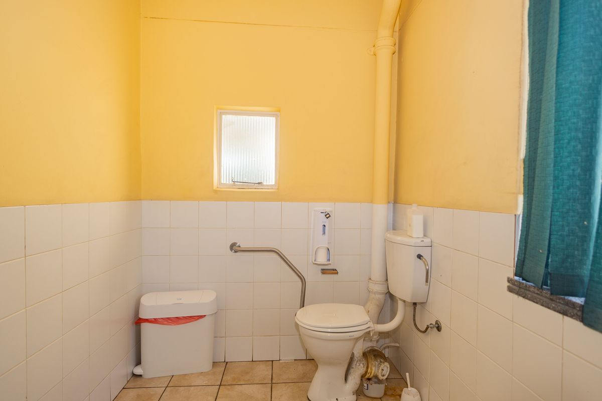 A functional commercial bathroom featuring tiled walls and flooring, a standard toilet, and a safety grab rail.