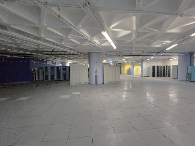 Large open-plan office space featuring a distinctive waffle slab ceiling, tiled flooring, and integrated server cabinets, offering a versatile commercial layout.