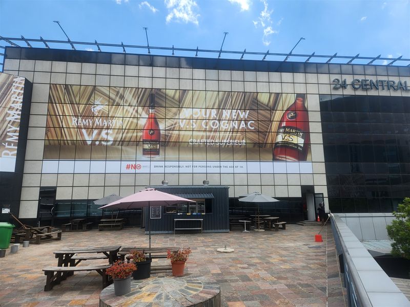 An outdoor patio area featuring stone paving and a large commercial building facade with prominent advertising signage.
