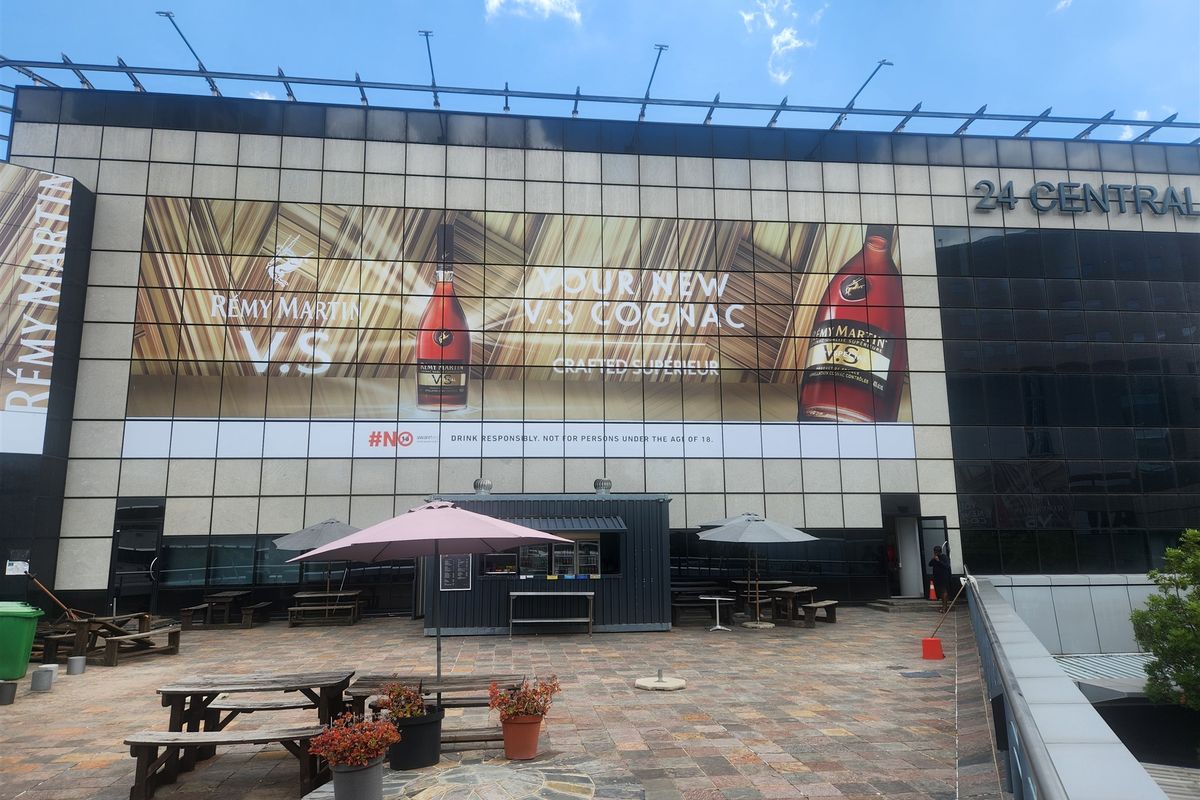 An outdoor patio area featuring stone paving and a large commercial building facade with prominent advertising signage.