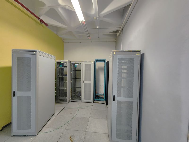A functional server room featuring a raised floor, exposed ceiling with fire suppression systems, and multiple server rack enclosures.