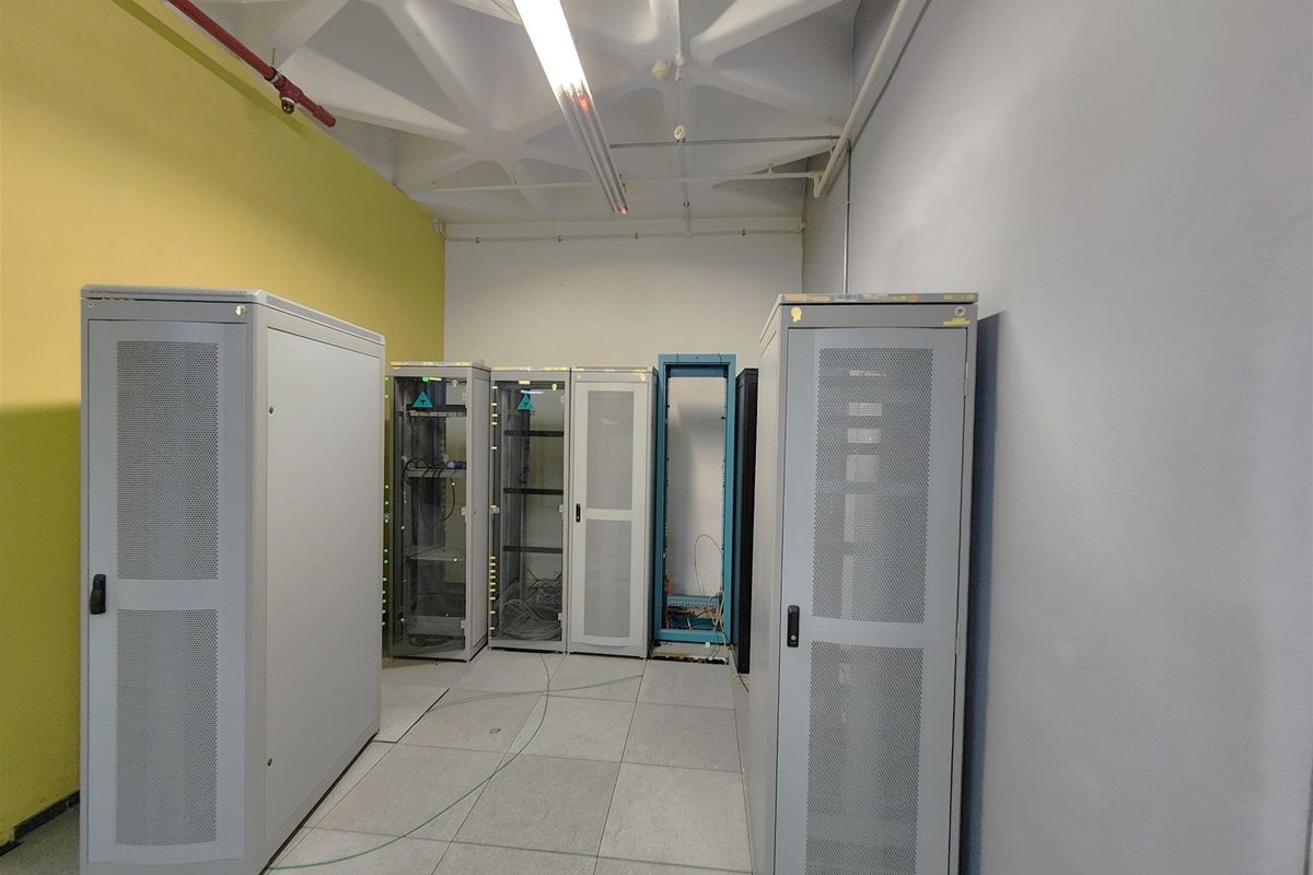 A functional server room featuring a raised floor, exposed ceiling with fire suppression systems, and multiple server rack enclosures.
