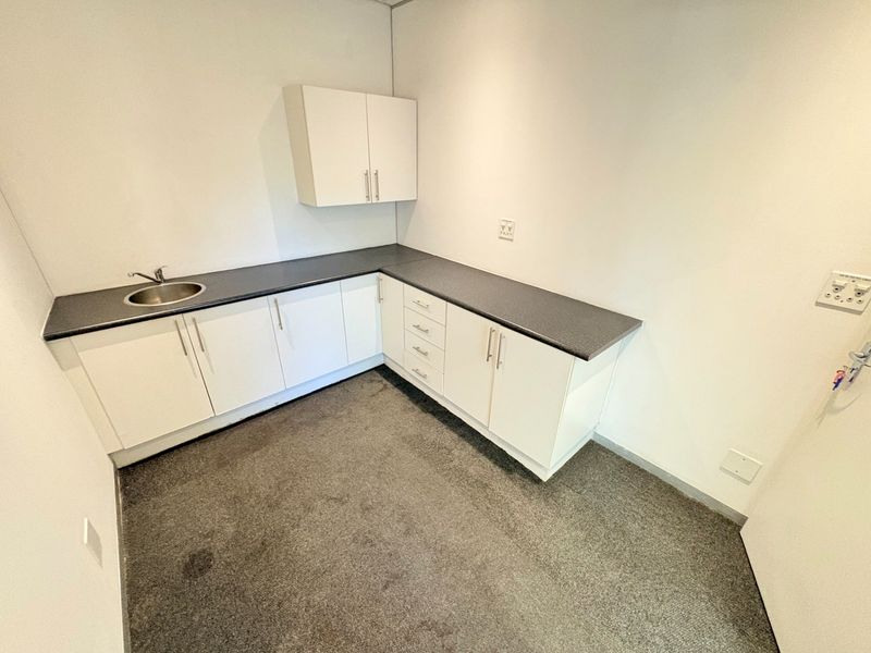 A compact office kitchenette featuring white built-in cabinetry, dark laminate countertops, and a stainless steel sink.