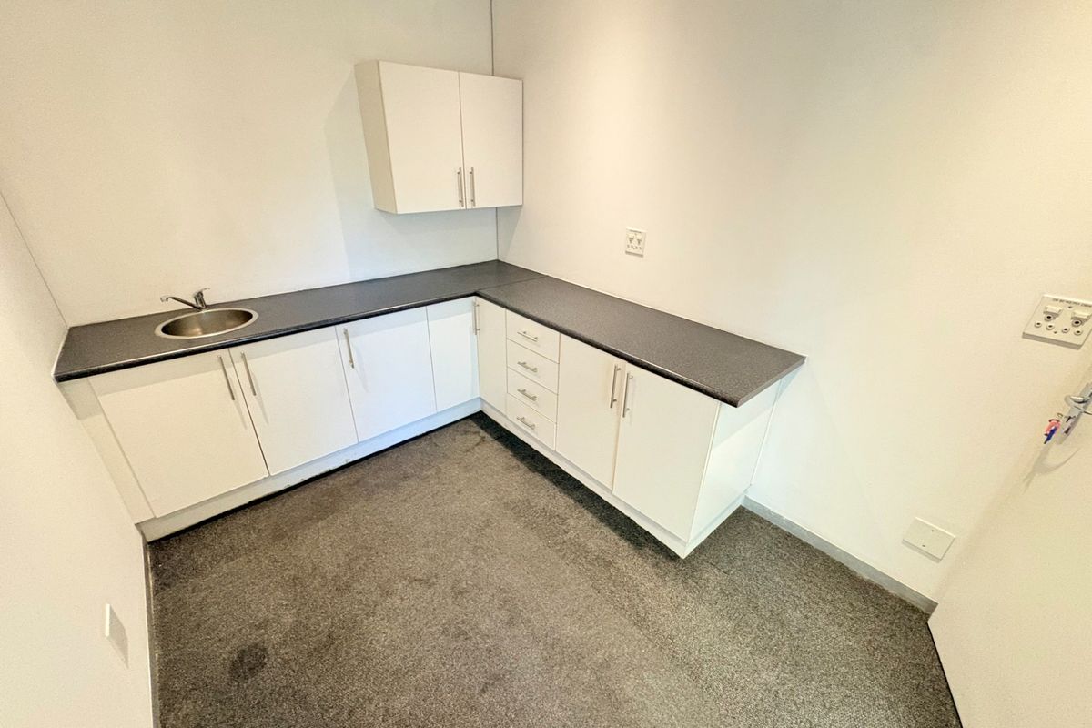 A compact office kitchenette featuring white built-in cabinetry, dark laminate countertops, and a stainless steel sink.