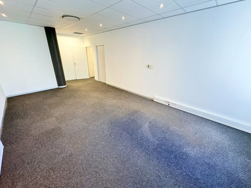 A vacant office space featuring a suspended ceiling with recessed lighting, carpeted flooring, and a prominent structural column.