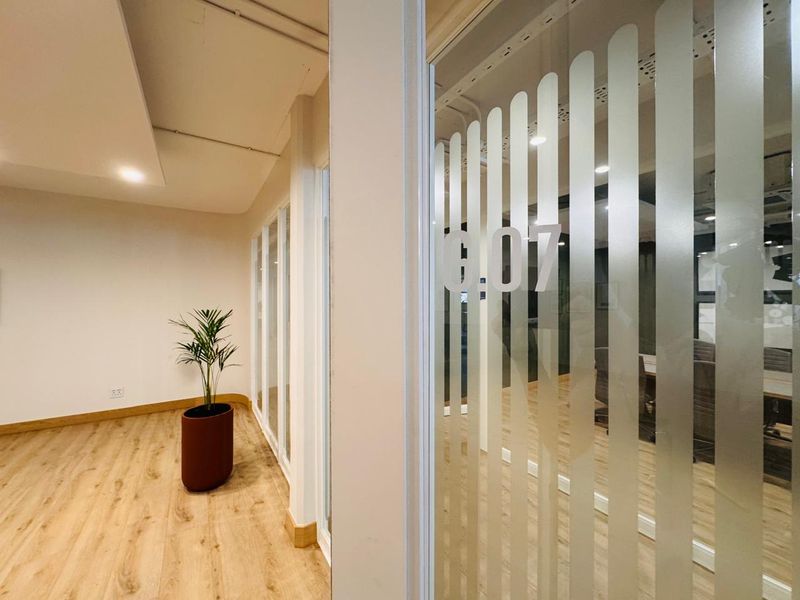 Modern office corridor featuring glass partitions with frosted privacy film and high-quality laminate flooring in a well-maintained professional workspace.