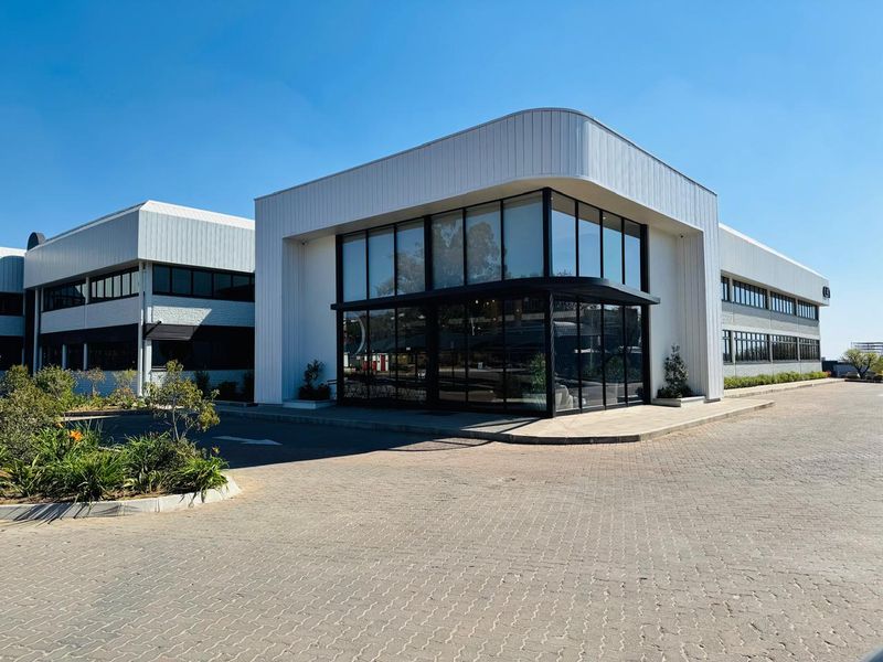 Modern office building exterior featuring extensive glass curtain walling, metal cladding, and a paved driveway entrance.