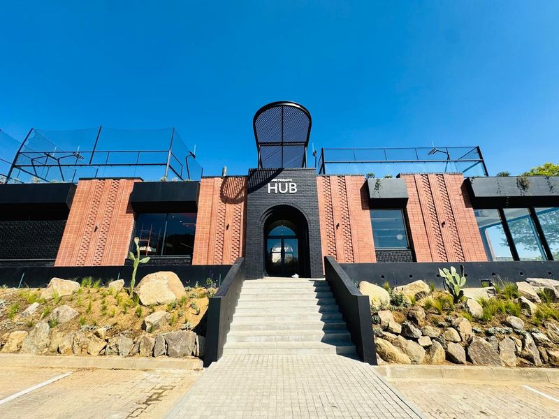 Modern office building exterior featuring a striking brick facade, arched entrance, and landscaped stone retaining wall with a paved staircase leading to the main entry.
