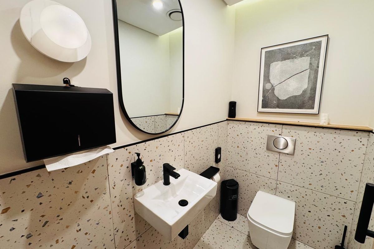 Modern office bathroom featuring terrazzo-style tiling, a wall-mounted basin with black fixtures, and a wall-hung toilet with a concealed cistern.