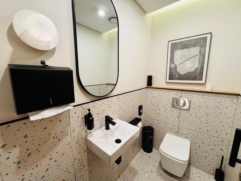 Modern office bathroom featuring terrazzo-style tiling, a wall-mounted basin with black fixtures, and a wall-hung toilet with a concealed cistern.