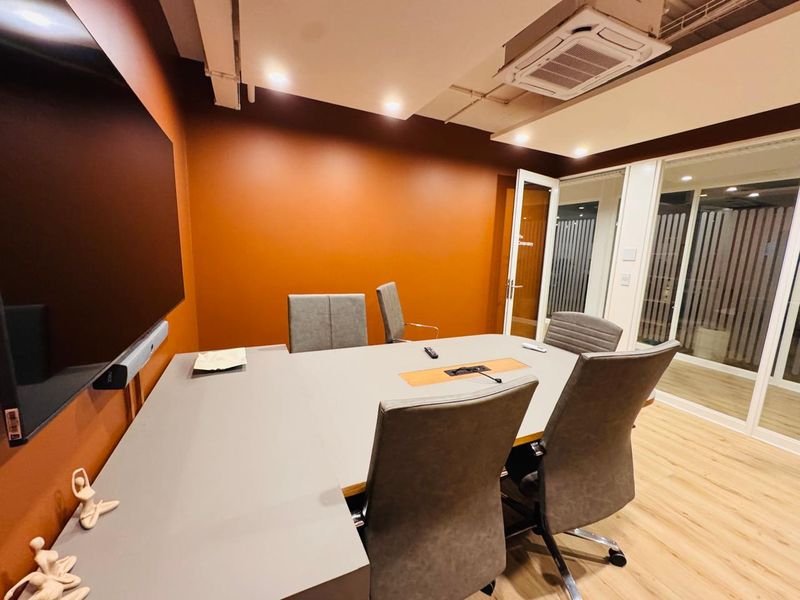 A modern, well-lit office meeting room featuring a large conference table, glass partitions, and integrated ceiling air conditioning.