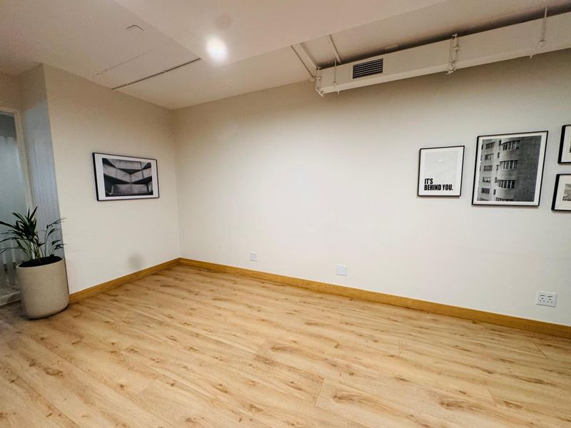 A bright, empty office space featuring modern laminate flooring, exposed ceiling ducting, and clean white walls, suitable for a professional workspace.