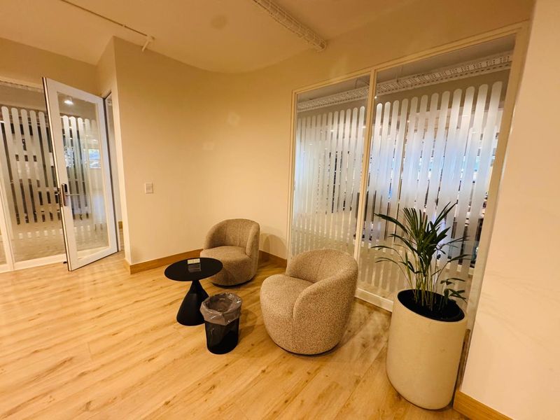 A modern office waiting area featuring light wood-look flooring, frosted glass partitions for privacy, and clean, neutral wall finishes.