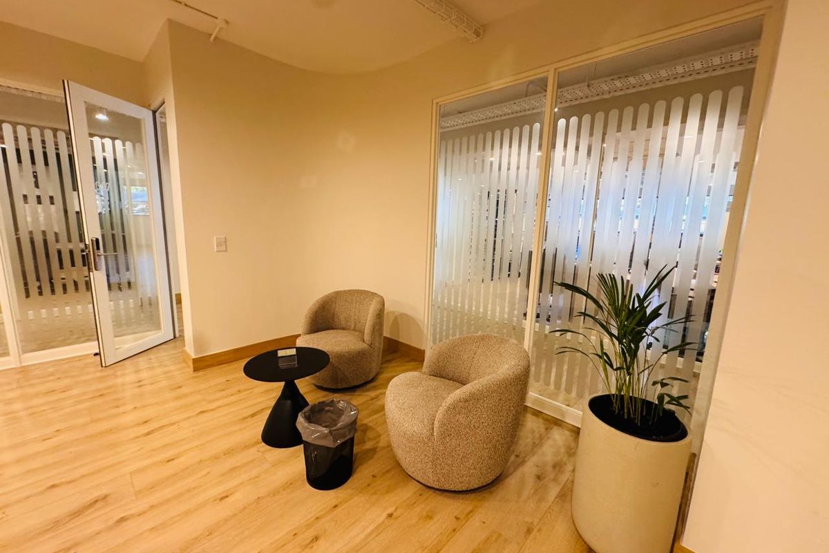 A modern office waiting area featuring light wood-look flooring, frosted glass partitions for privacy, and clean, neutral wall finishes.