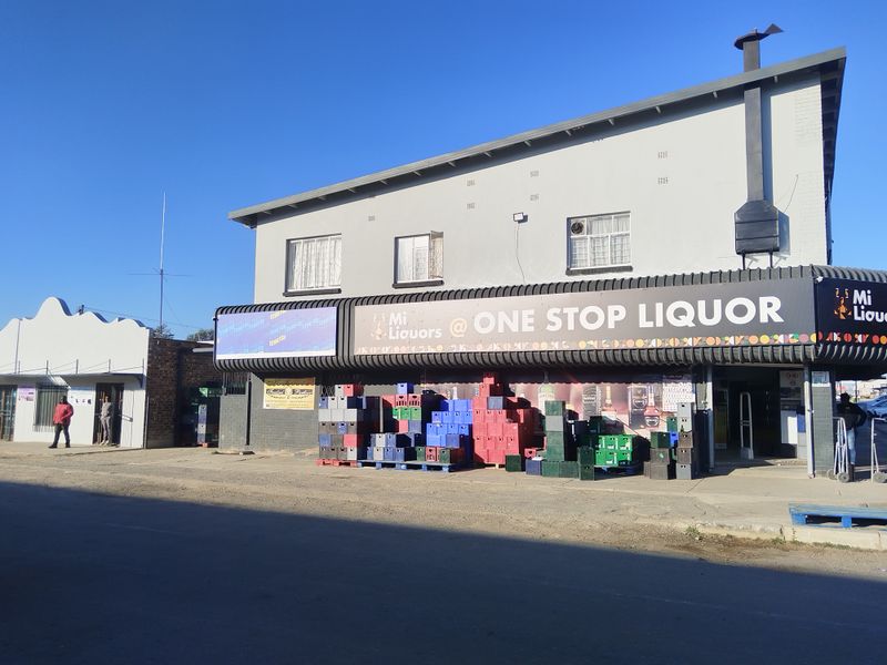 Front elevation of a commercial property featuring prominent signage, security bars on windows, and an external chimney stack.