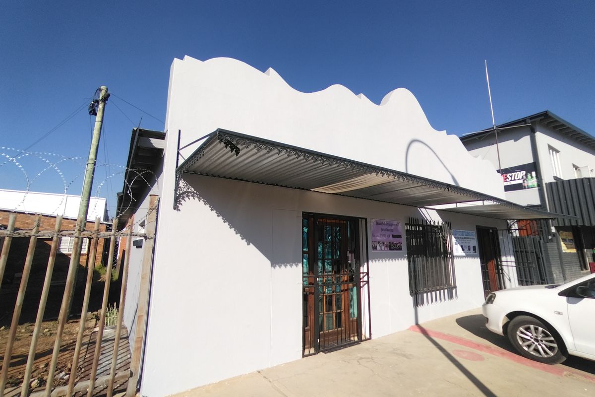 Front facade of a commercial building featuring a decorative parapet, corrugated metal awning, and security installations including bars and gates.