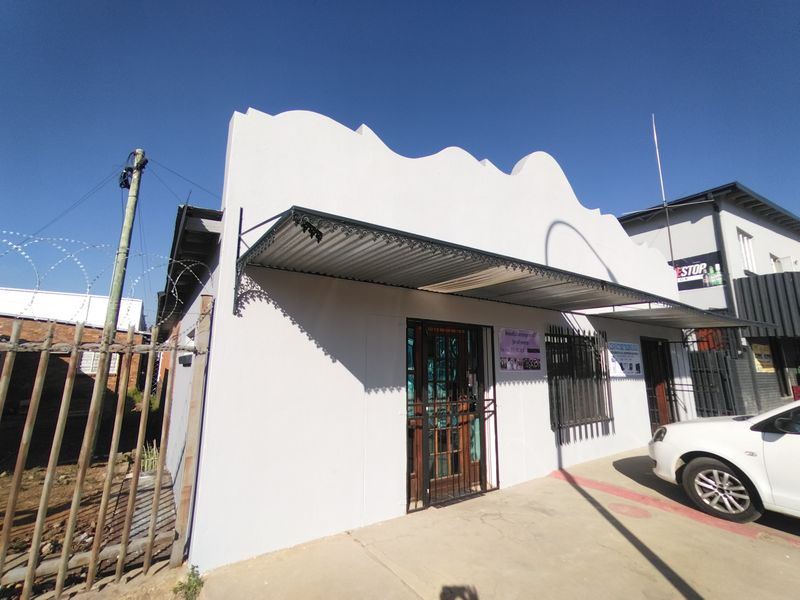 Front facade of a commercial building featuring a decorative parapet, corrugated metal awning, and security installations including bars and gates.