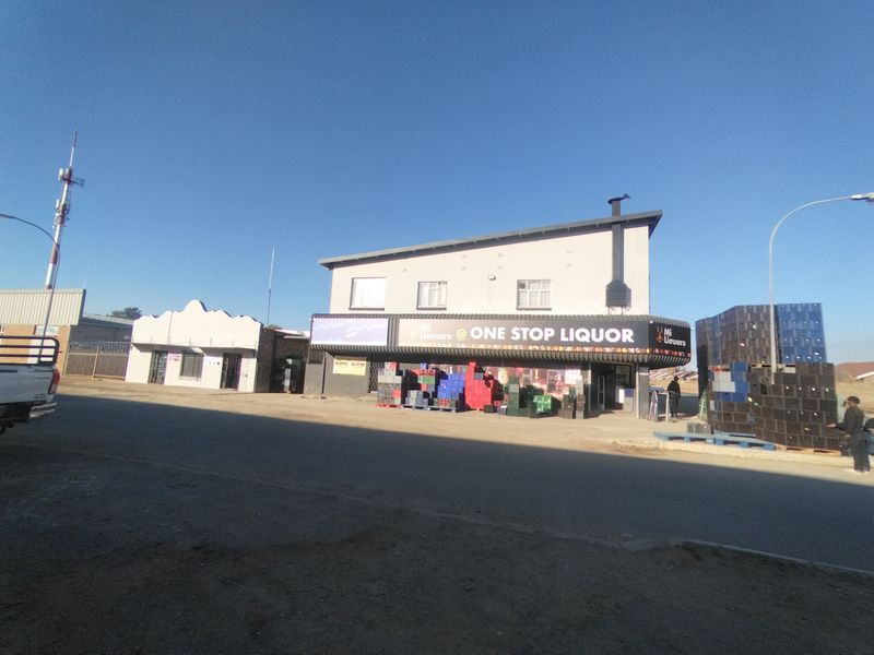 Front exterior view of a commercial liquor store building featuring prominent signage, a paved forecourt, and an external chimney structure.
