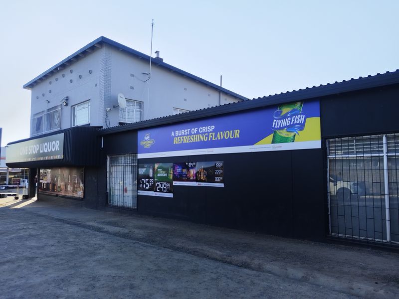 Front exterior view of a commercial liquor store building featuring prominent signage, security bars on windows, and a corrugated metal roof.