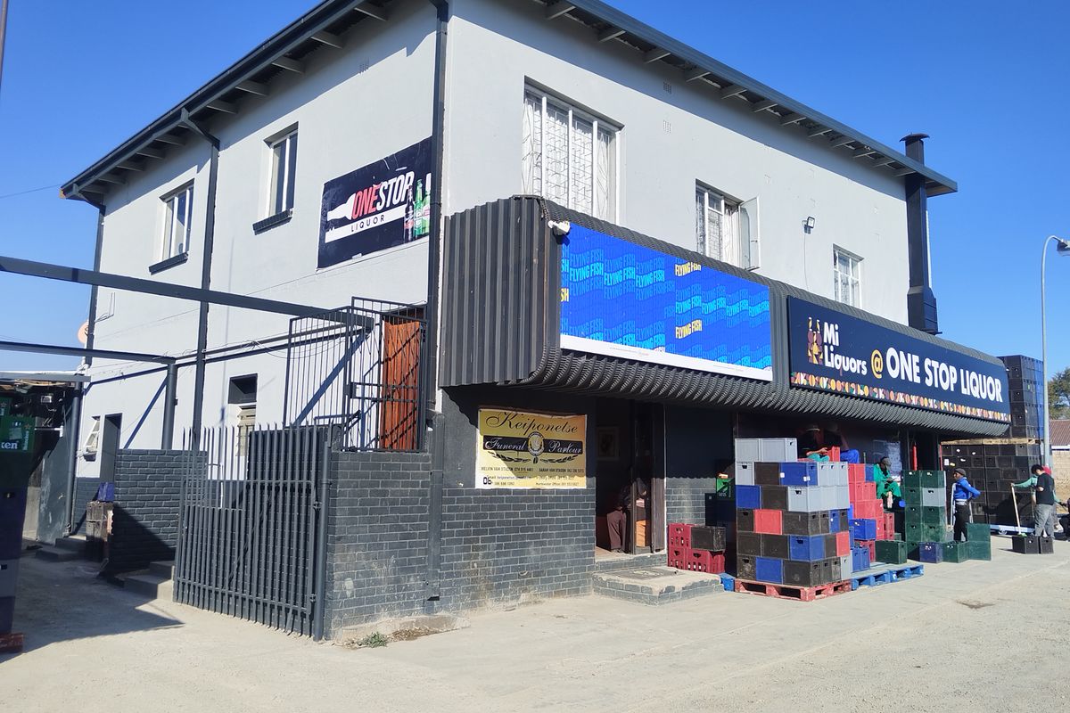 Commercial building exterior featuring a retail storefront with signage, metal security fencing, and a paved entrance area.